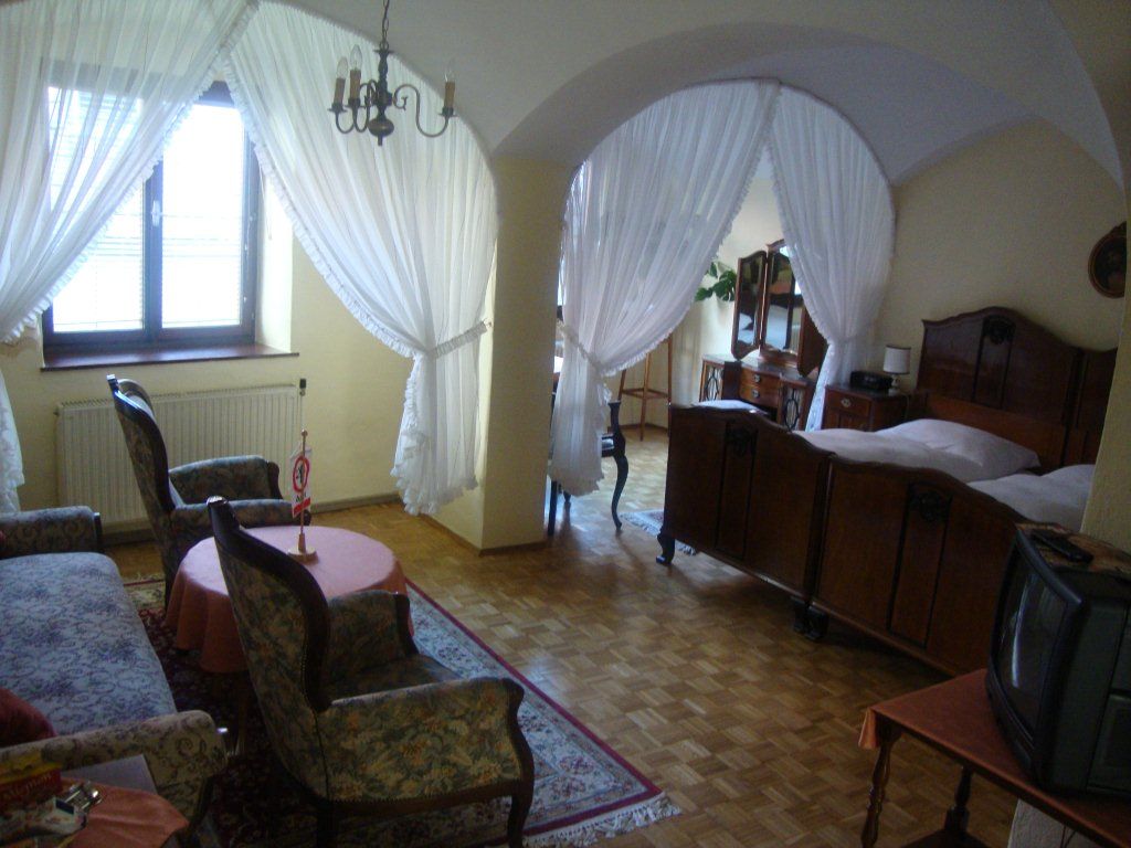 Útulný pokoj pro hosty se starožitným nábytkem, manželskou postelí, křesly a malou TV. Spací část je oddělena závěsy.