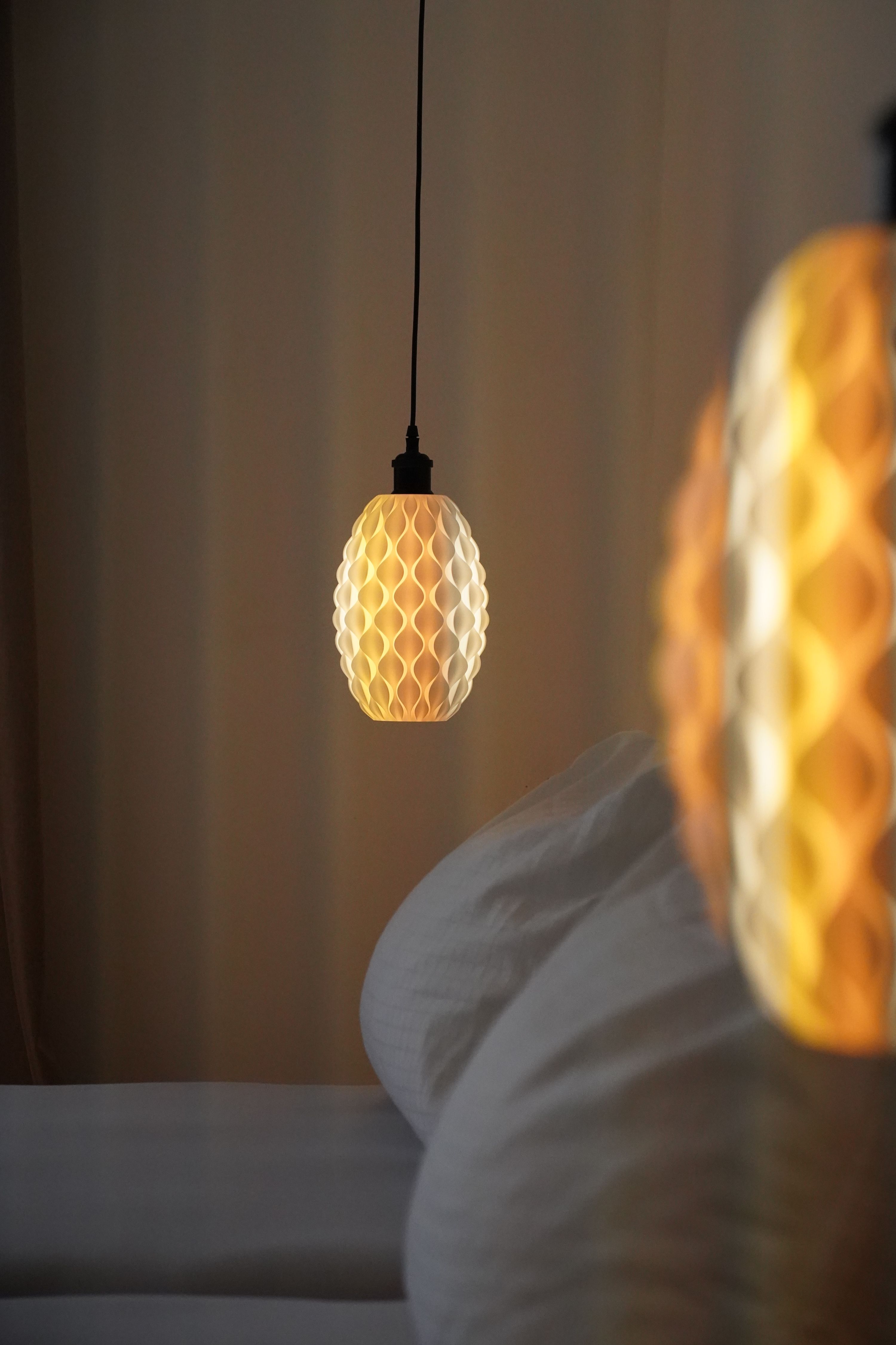 Detailní záběr na závěsnou lampu se vzorem včelí plástve, která vyzařuje teplé světlo vedle postele.