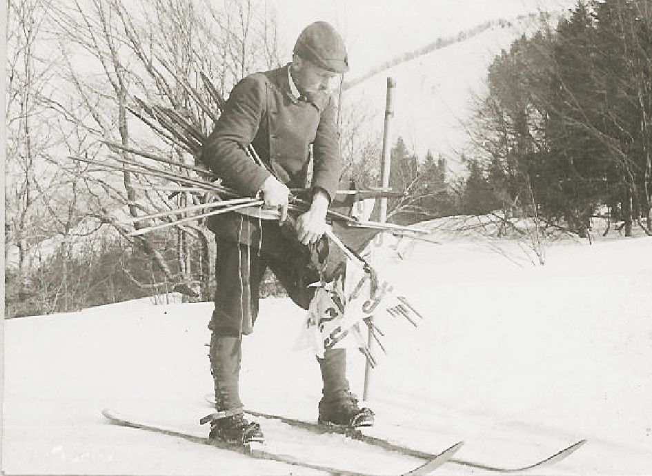 Historická fotografie muže na lyžích s lyžařskými hůlkami na sněhu.