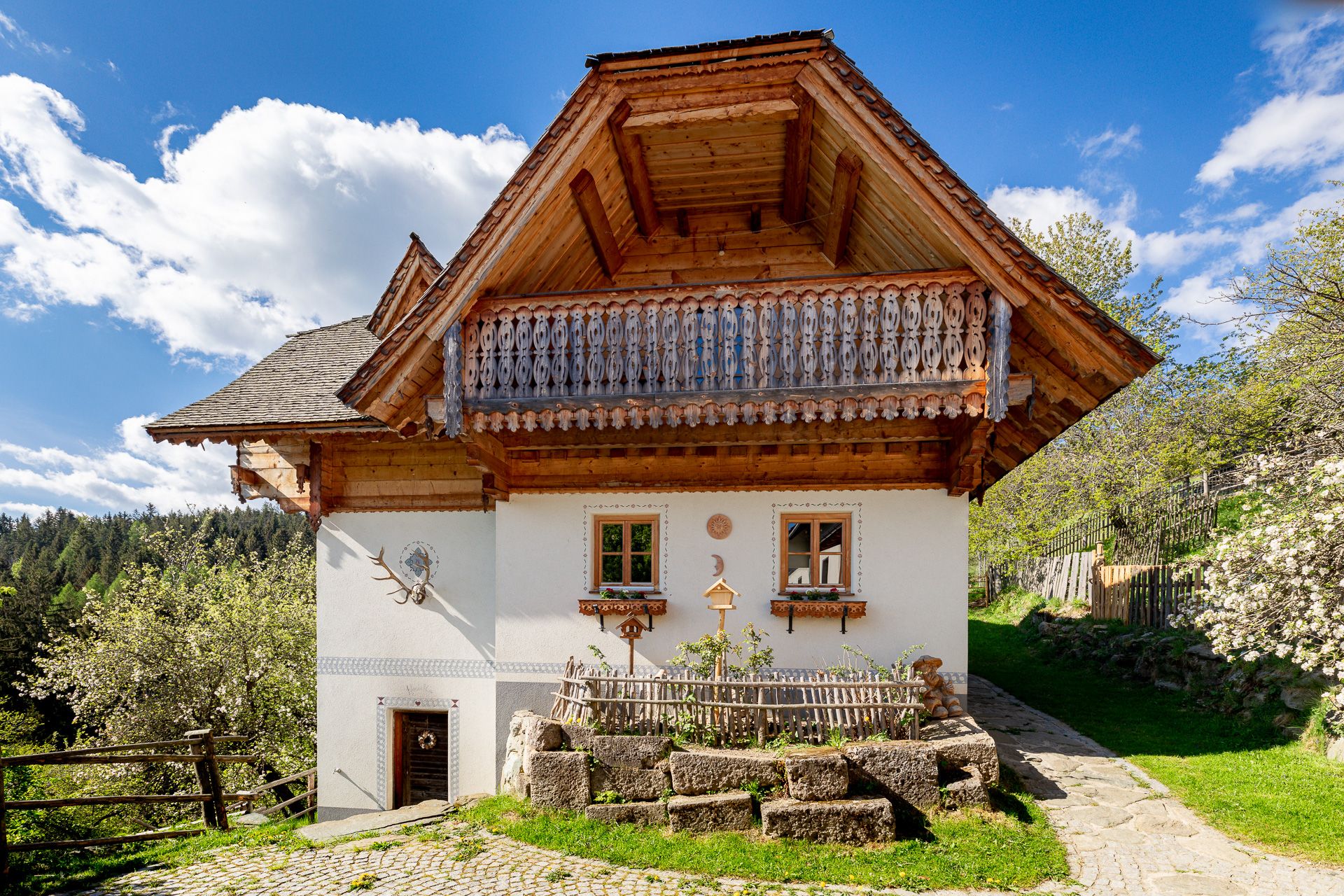 Tradiční dům s dřevěným balkonem a bílou fasádou, obklopený přírodou.