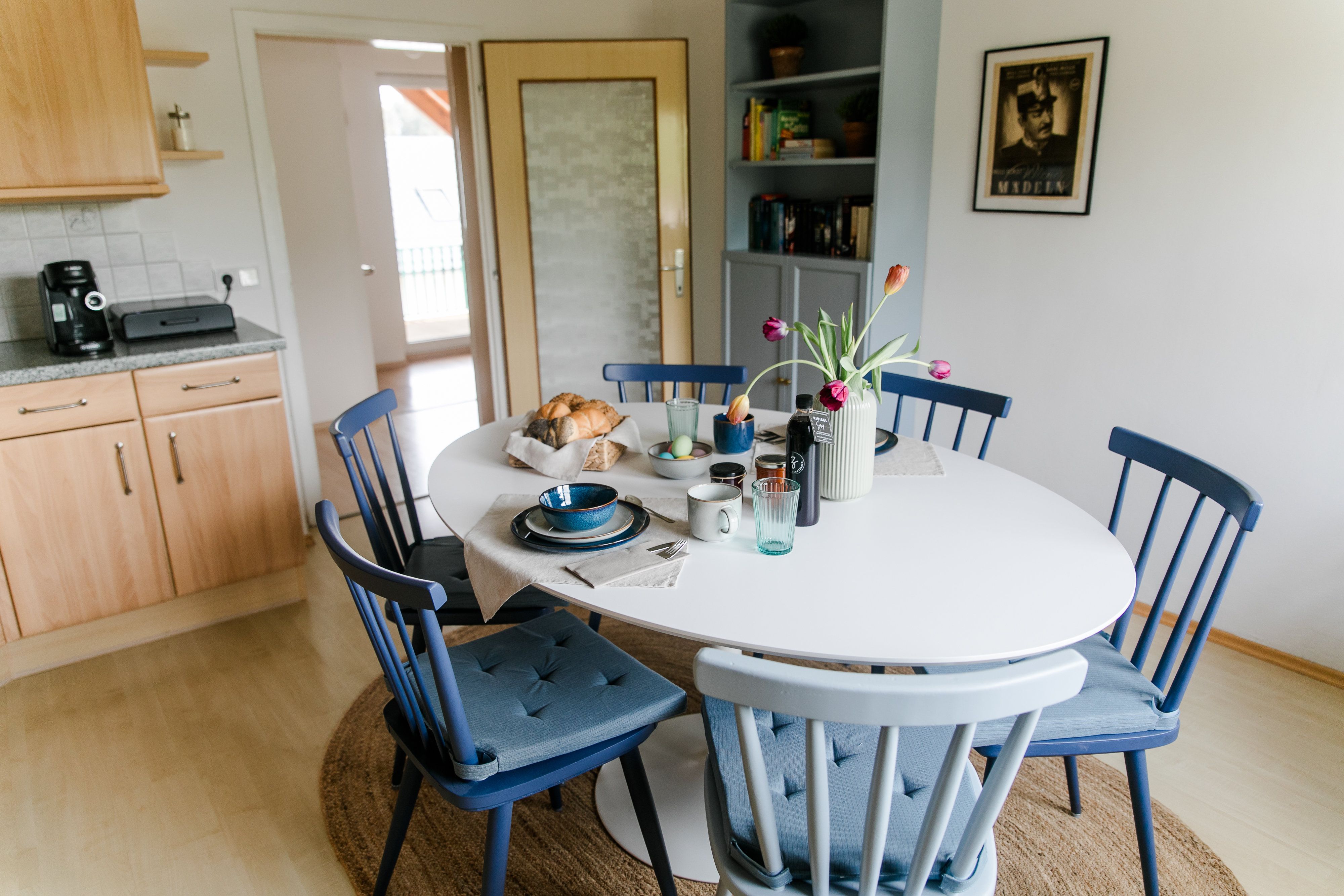 Jídelní kout v kuchyni s kulatým stolem, modrými židlemi a snídaňovým stolem.