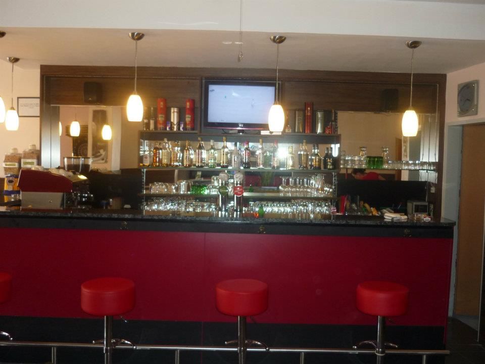 Pohled do interiéru baru s červenými stoličkami a osvětlenými policemi plnými lahví.