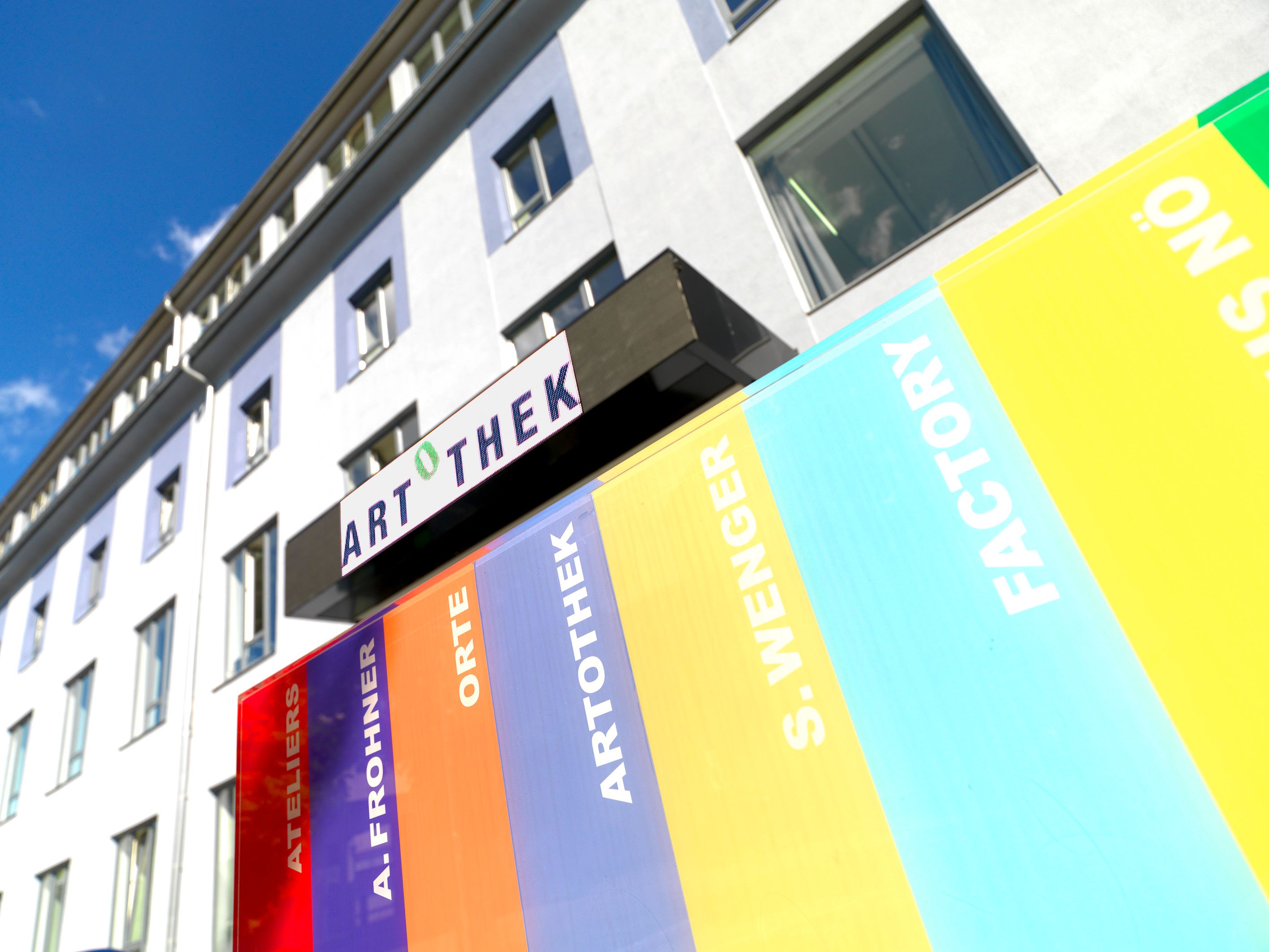 Pohled zvenčí na budovu s nápisem Artothek a barevnými pruhy.