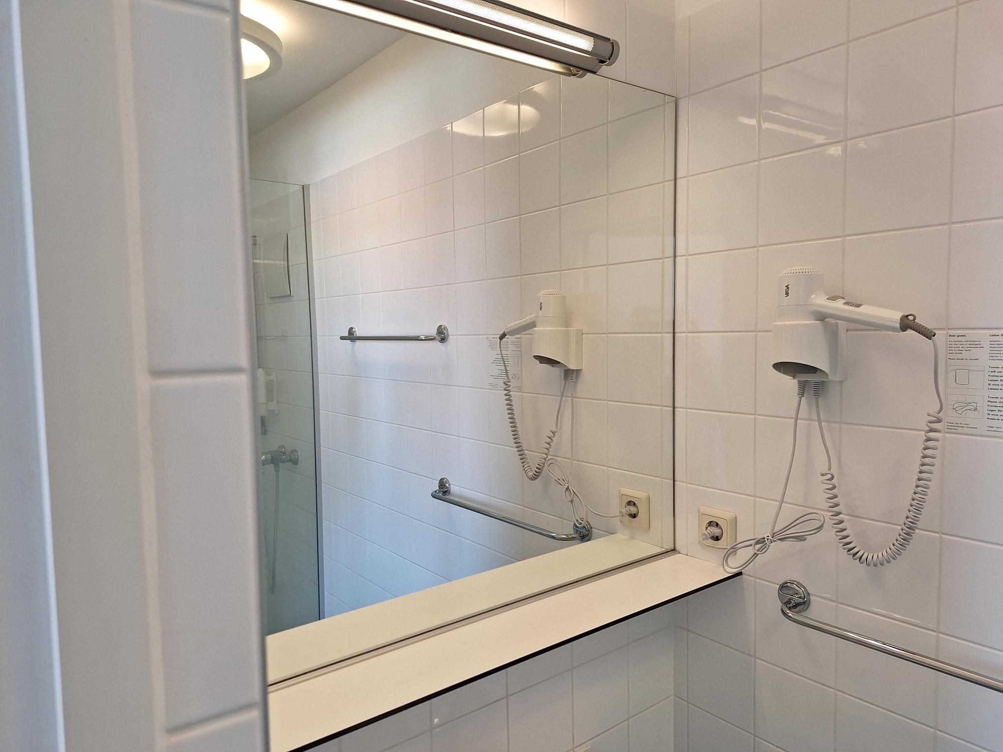 Moderní koupelna se zrcadlem, fénem a věšákem na ručníky.