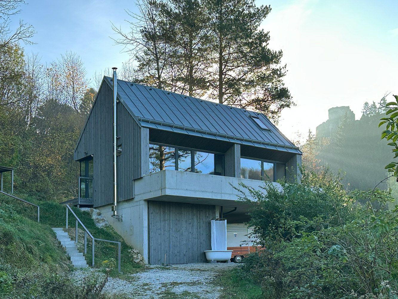 Moderní dům s dřevěnou fasádou a velkými okny v zalesněném prostředí.