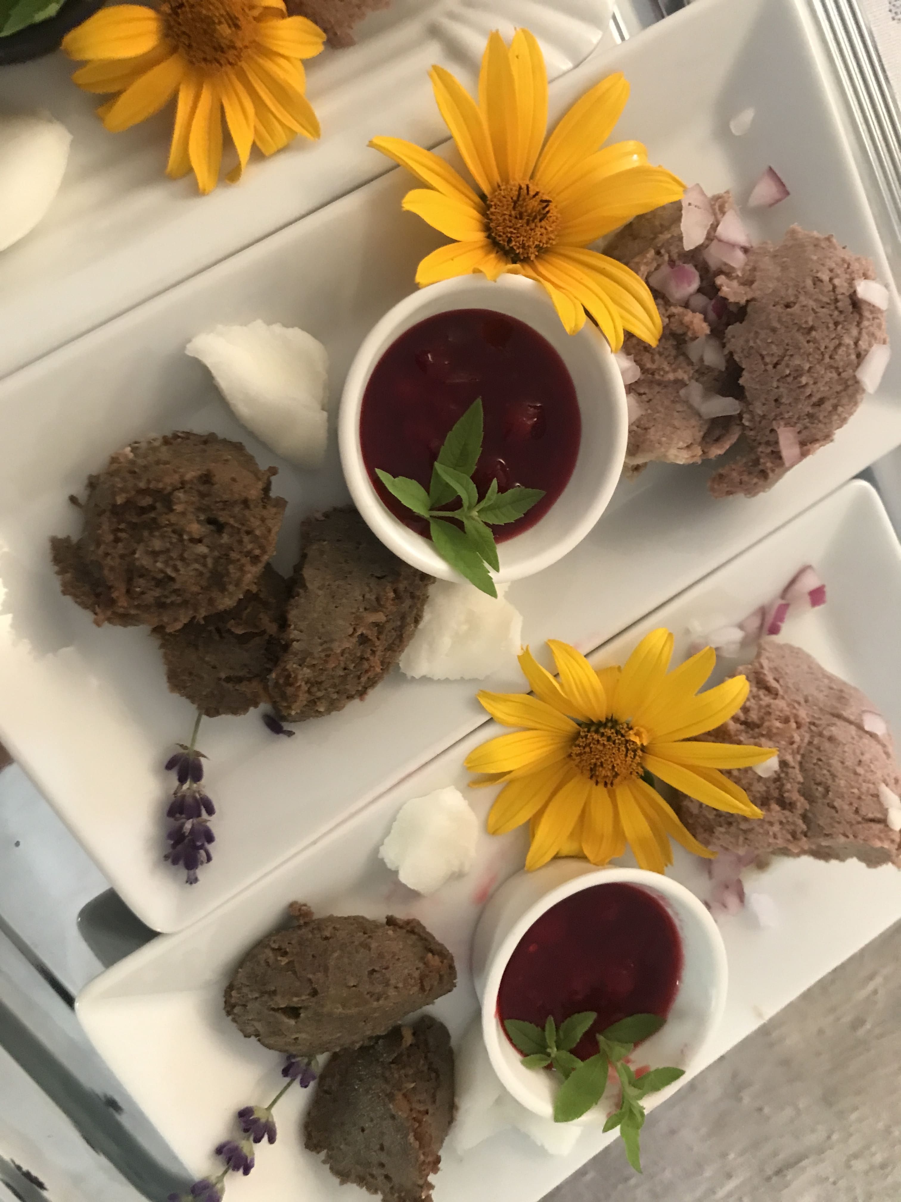 Talíře s pomazánkami, žlutými květy a červenými omáčkami v malých miskách.