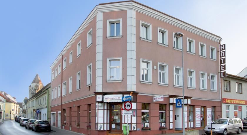 Třípatrová budova hotelu na rohu ulice s auty a obchody.