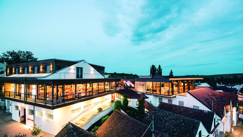 Moderní architektura vinařství za soumraku s osvětlenými interiéry a okolními budovami.