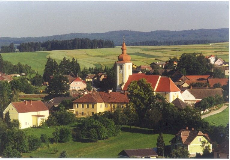 Letecký pohled na Waldkirchen an der Thaya s kostelem a okolními domy, obklopený poli a lesy.