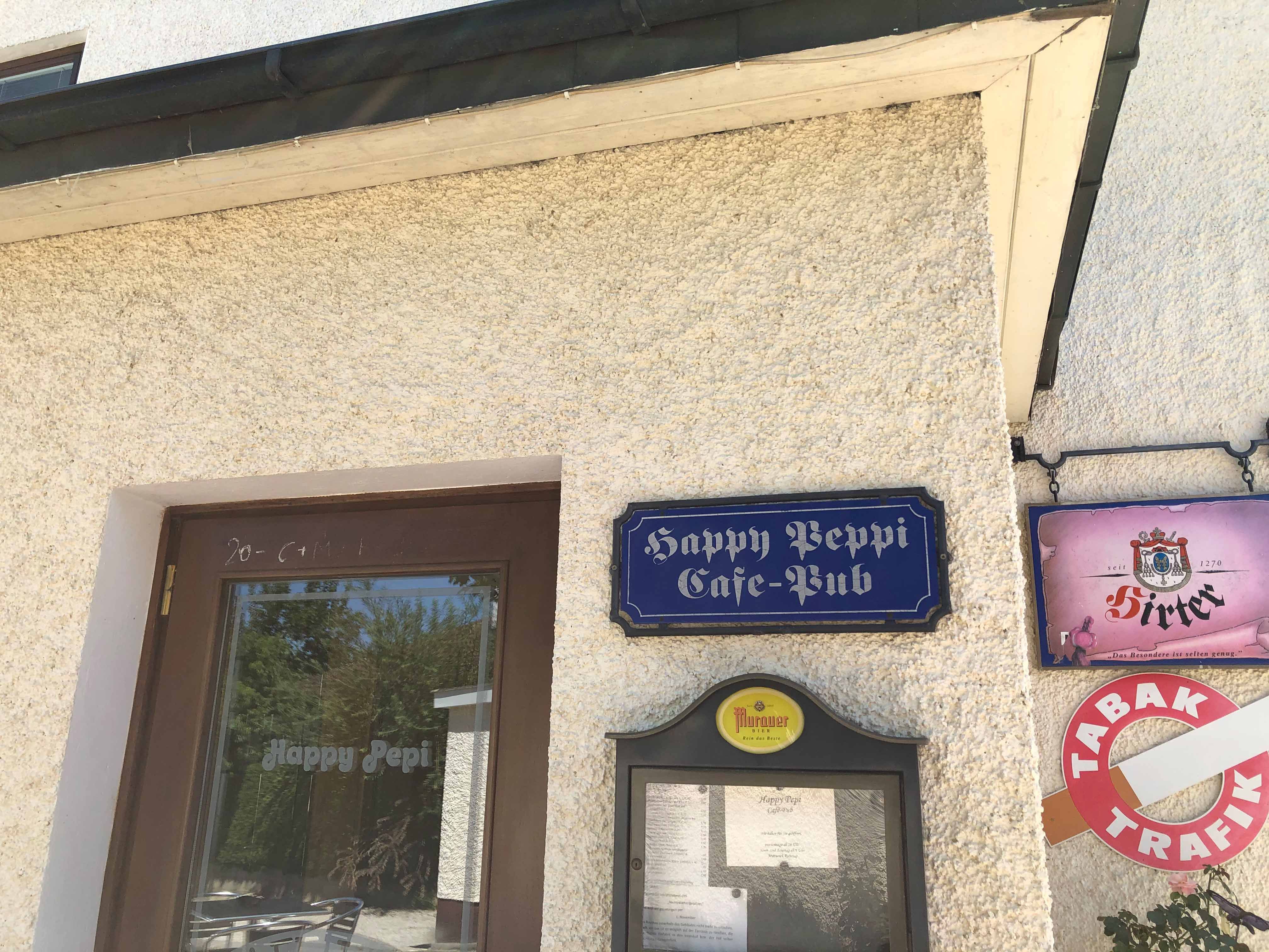 Vchod do kavárny Happy Pepi s nápisy a jídelním lístkem na stěně.