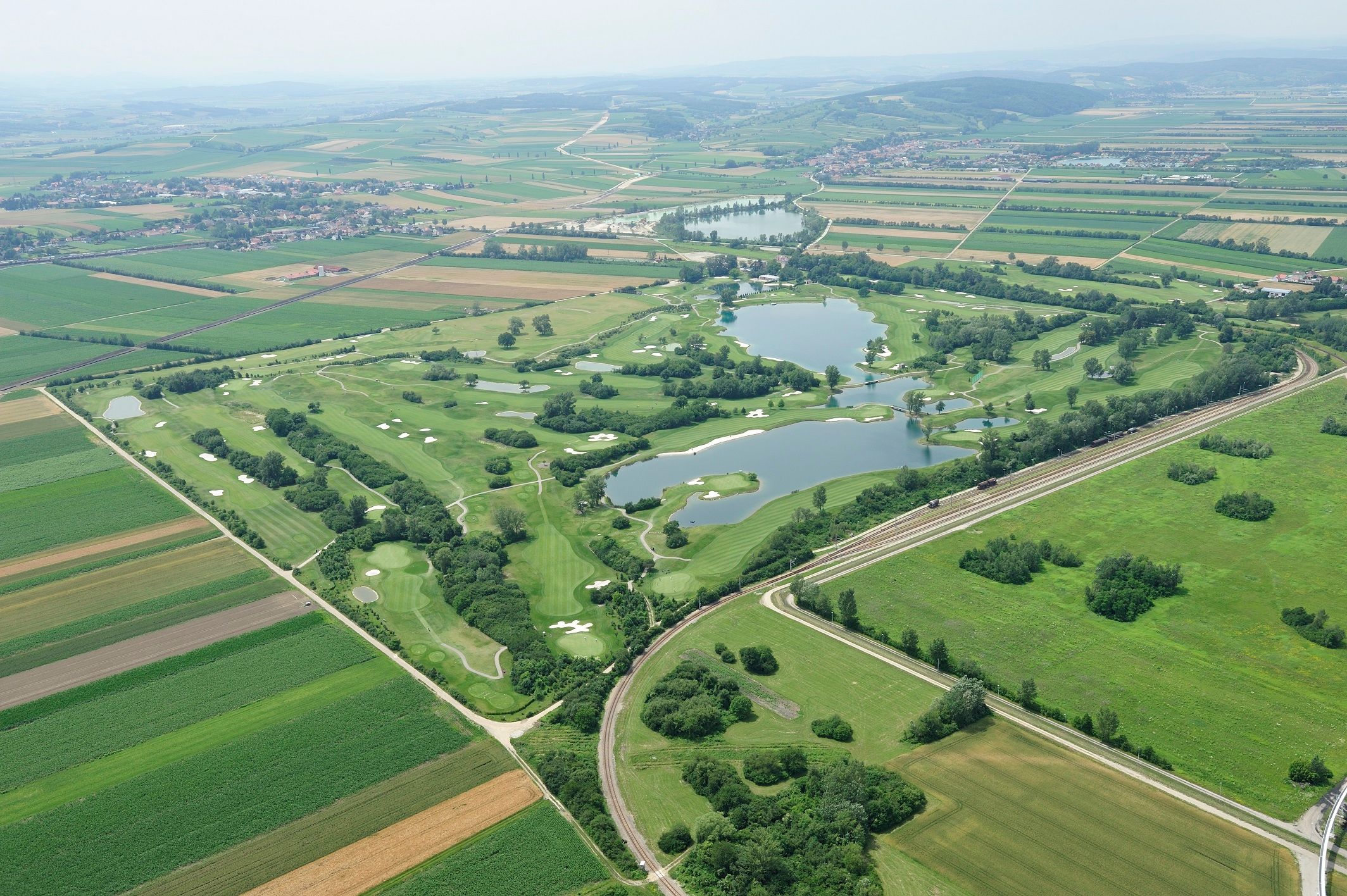 Letecký pohled na golfové hřiště s jezery a okolními poli.