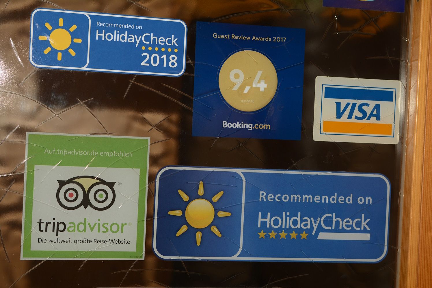 Samolepky HolidayCheck, Booking.com, TripAdvisor a Visa na skleněném povrchu.