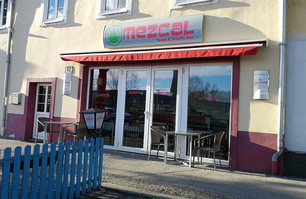 Exteriérový pohled na restauraci Mezcal s červenými markýzami a posezením.