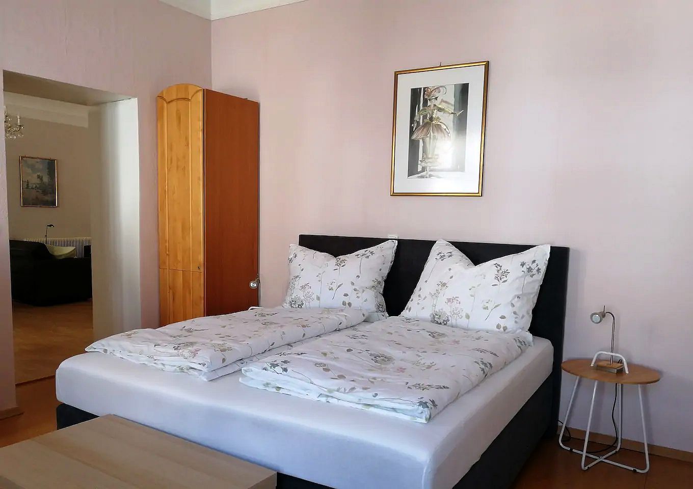 Ložnice s manželskou postelí, dřevěnou skříní a nástěnnou malbou.