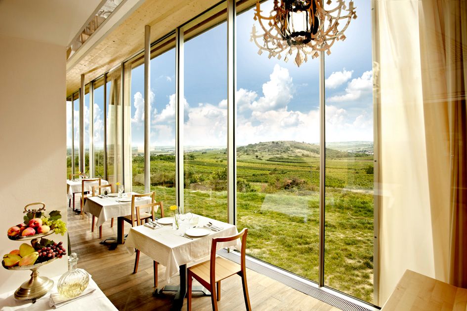 Pohled do interiéru restaurace s velkými okny a výhledem do zelené krajiny.