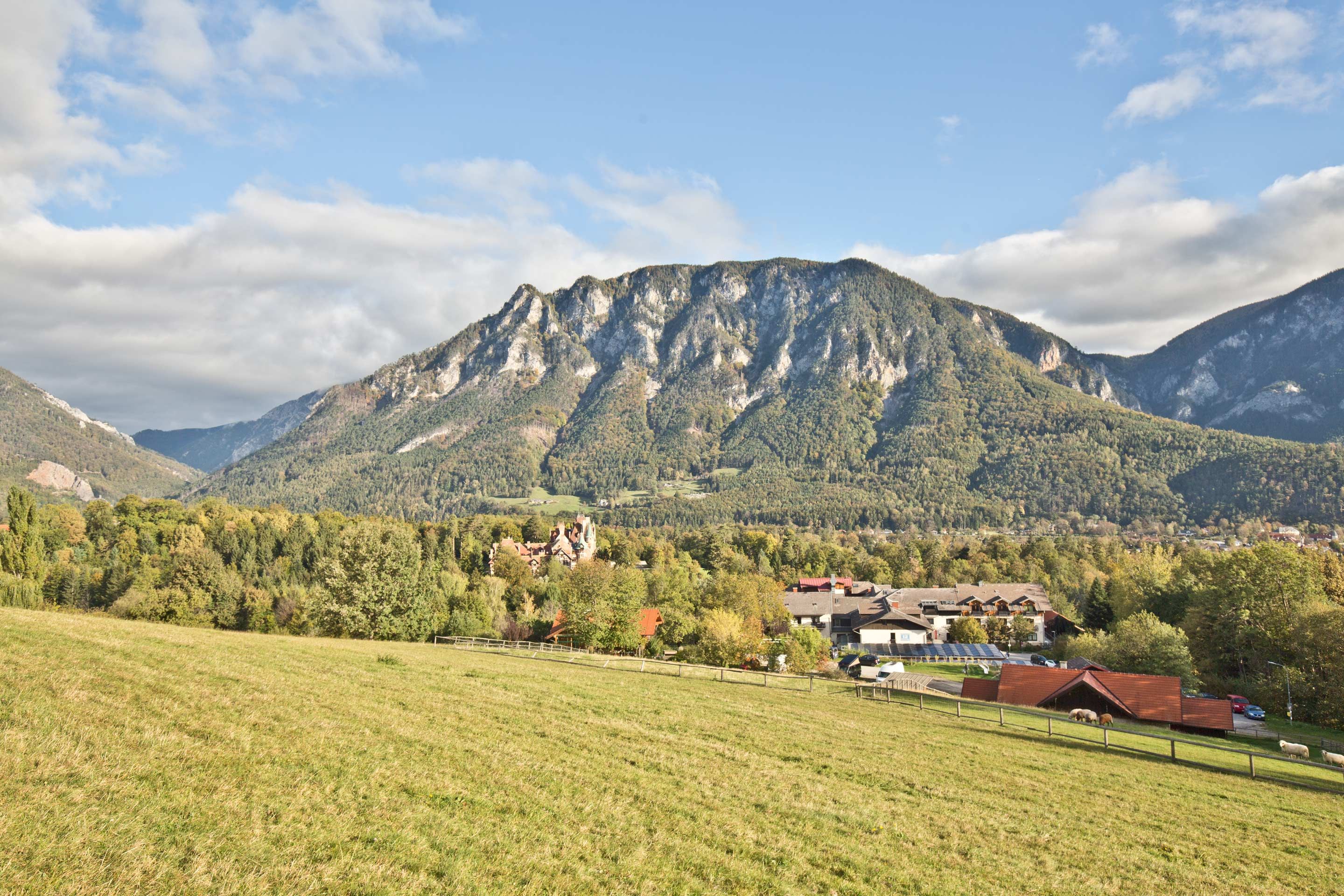 Panoramatický výhled na horskou krajinu s loukami v popředí a vesnicí v pozadí.