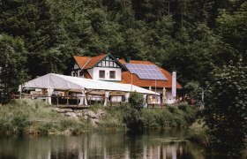 Hostinec se solárními panely a stanem na okraji lesa u rybníka.