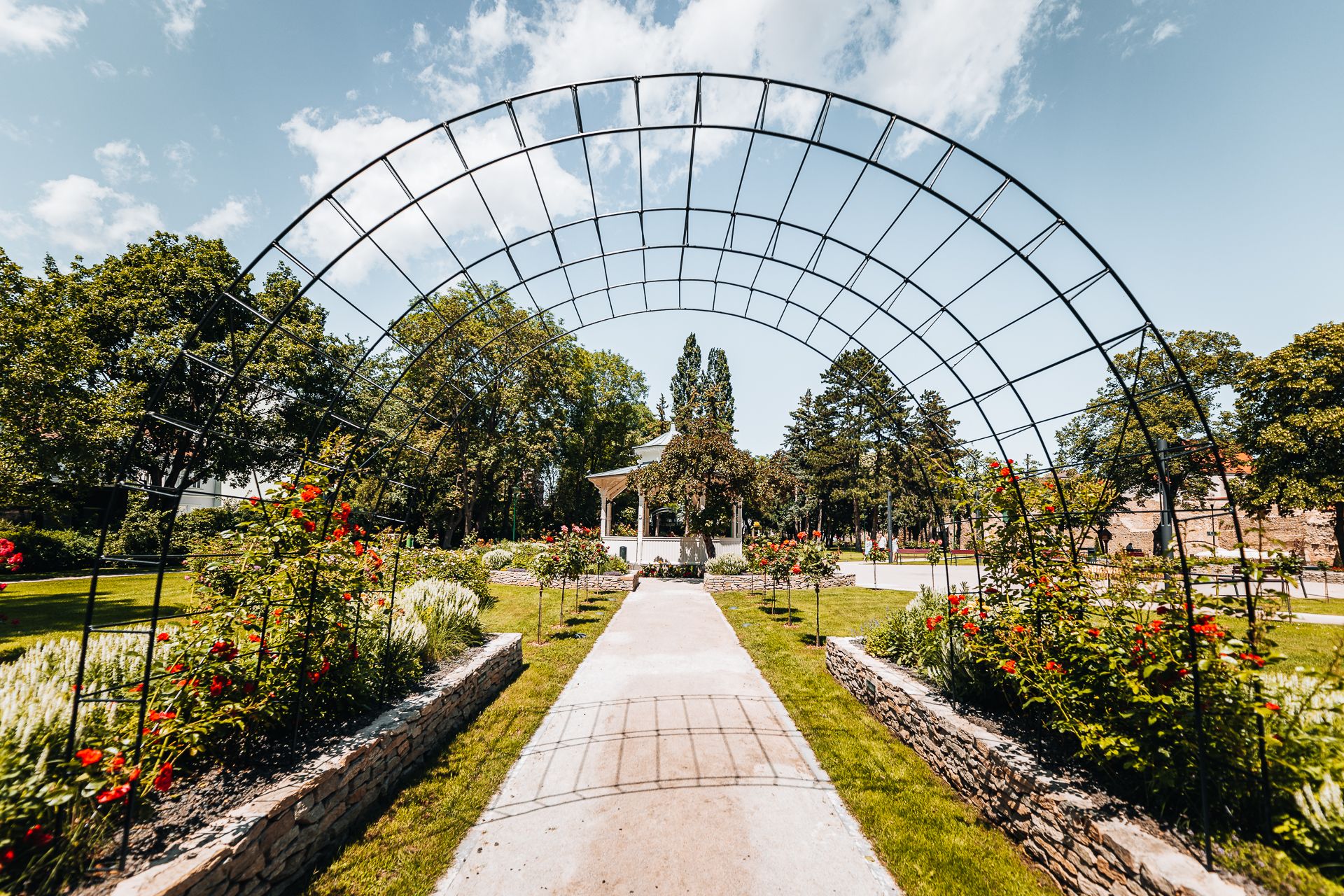 Zelený městský park s romantickým altánem, růžovou zahradou a klenutým obloukem