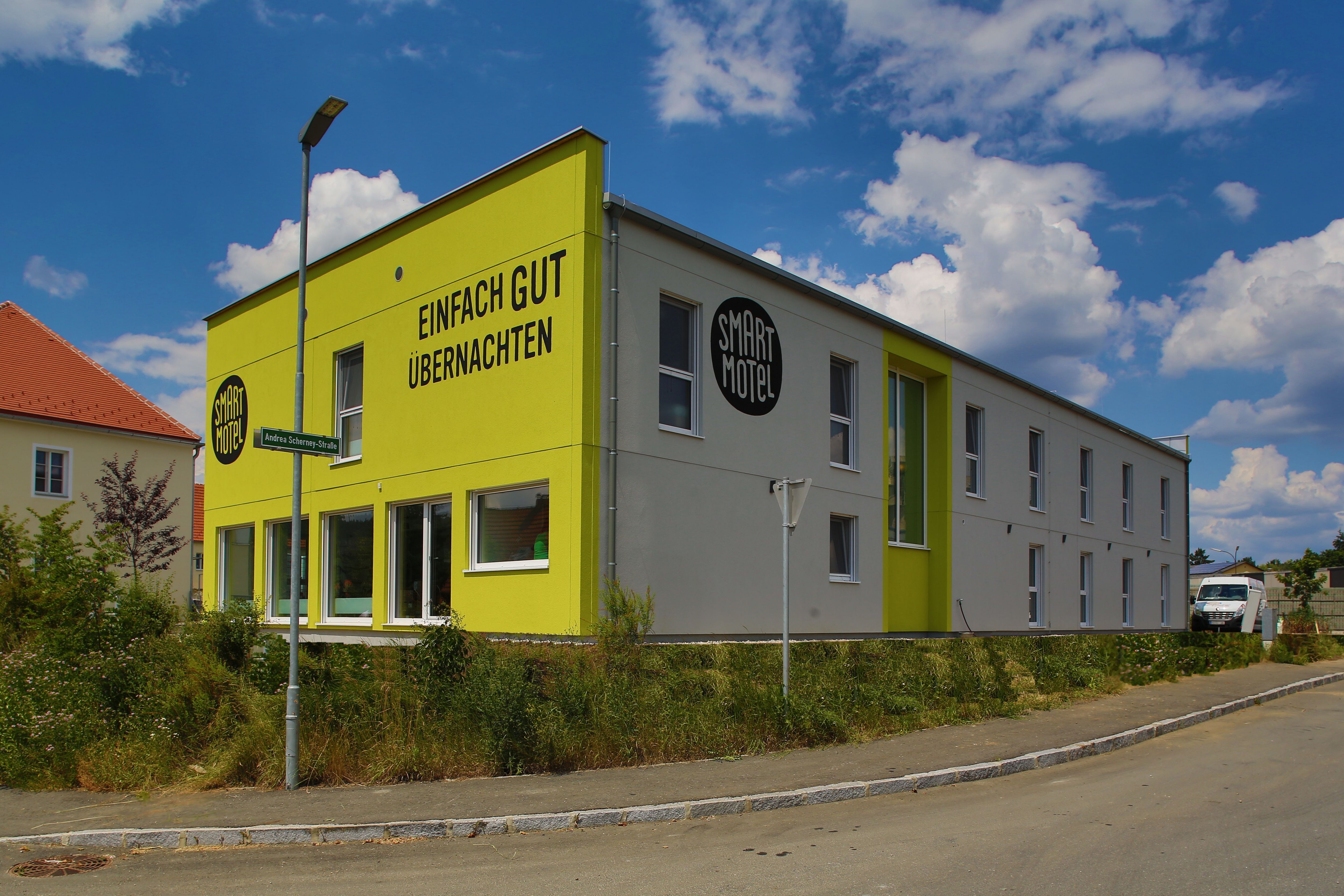 Pohled zvenčí na moderní dvoupatrový motel se žlutou fasádou a nápisem "Einfach gut übernachten".