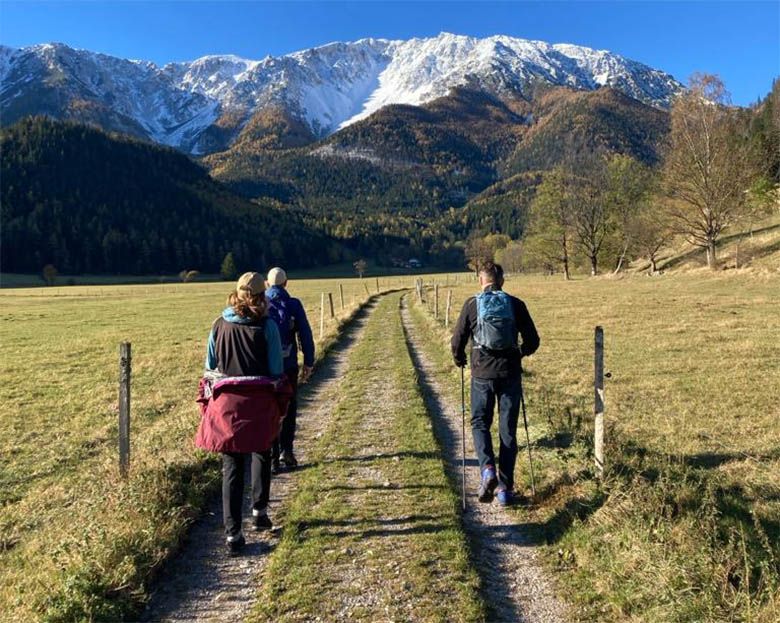 Čtyři turisté na polní cestě se zasněženými horami v pozadí.