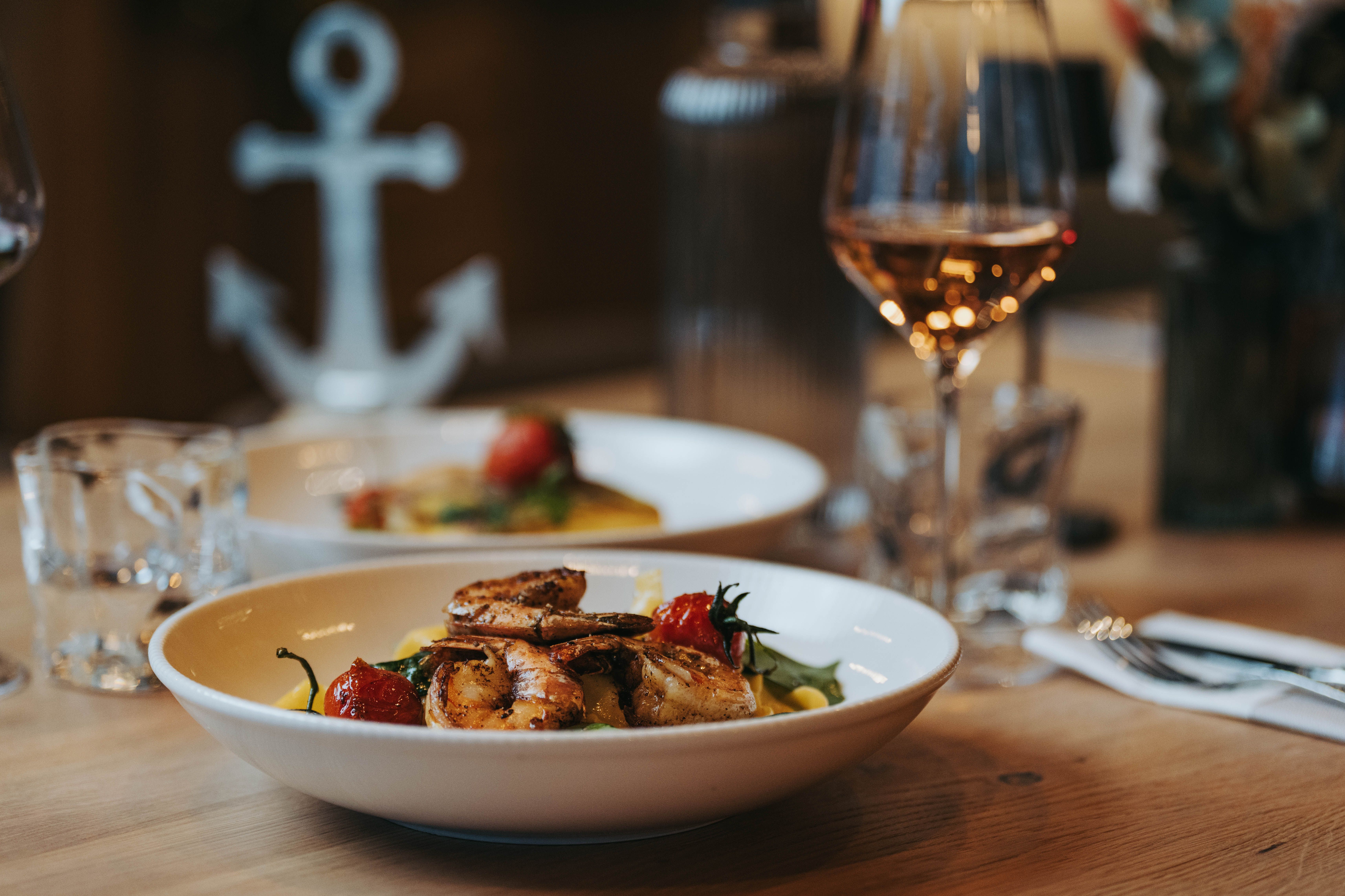 Talíř s krevetami a zeleninou na stole a vedle něj sklenka vína.