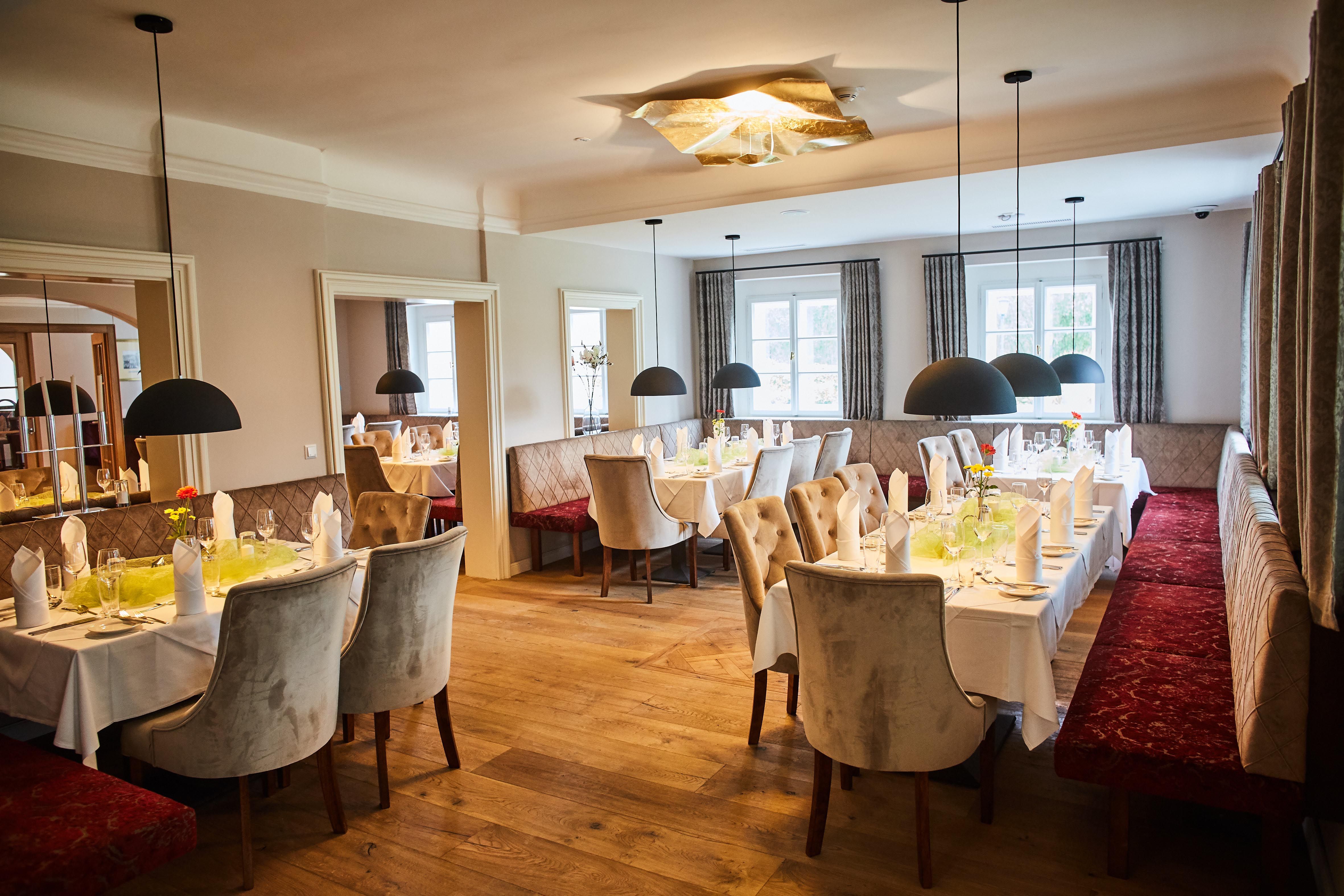 Elegantní restaurace s prostřenými stoly, čalouněnými lavicemi a závěsnými lampami na zámku Luberegg