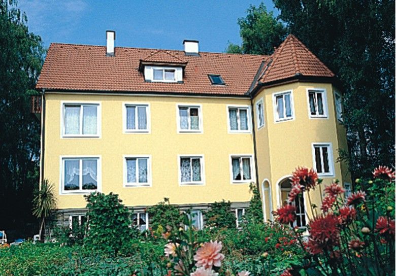 Žlutý dům s červenou střechou a zahradou v popředí.