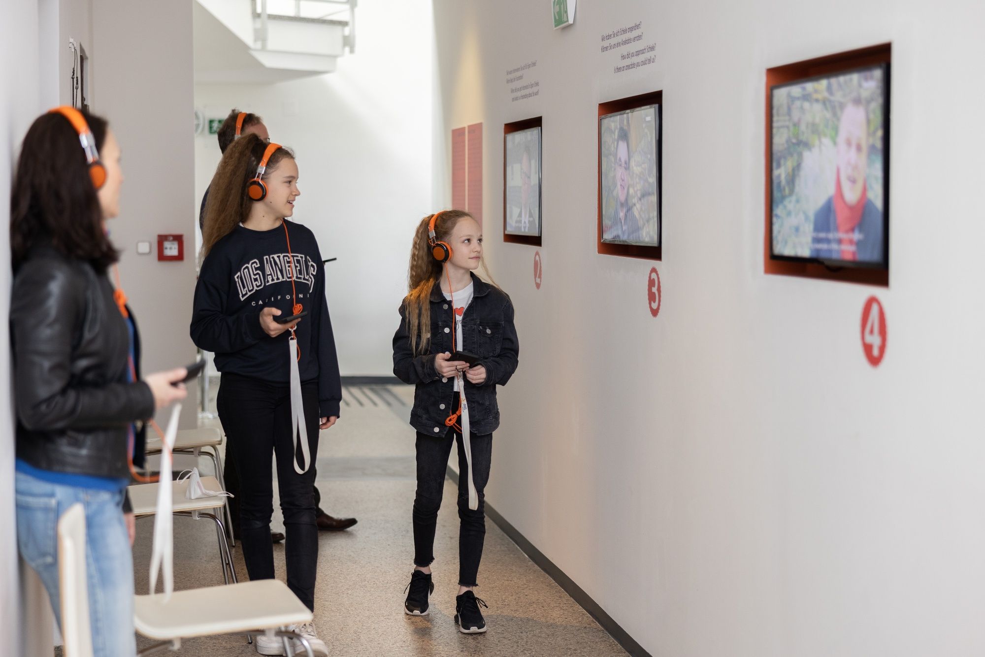 Návštěvníci se sluchátky na uších se dívají na obrazovky v muzeu.