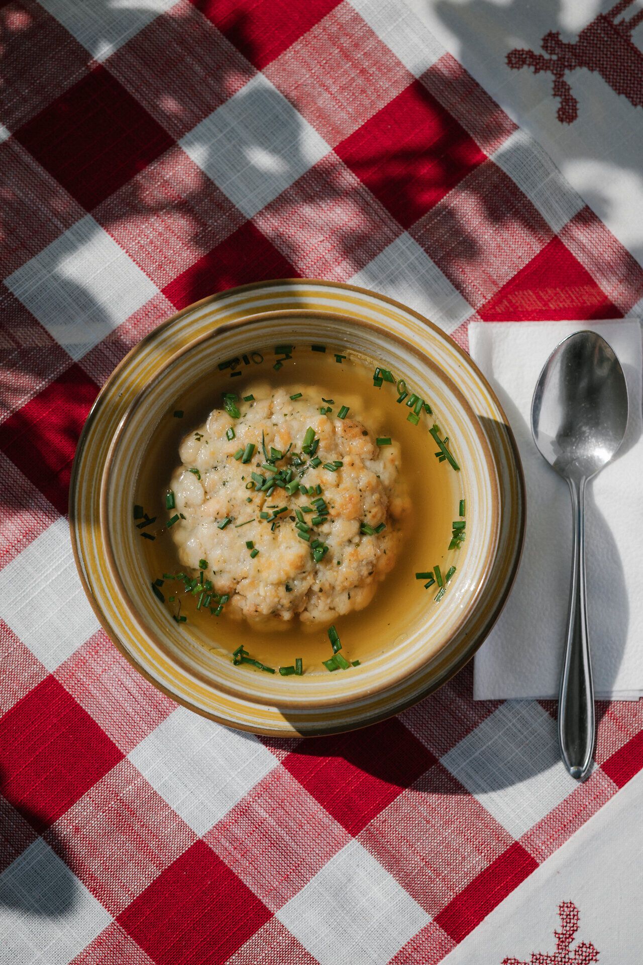 Čirá polévka s krupicovými knedlíčky na talíři na kostkovaném ubrusu v restauraci Damböckhaus u Schneebergu