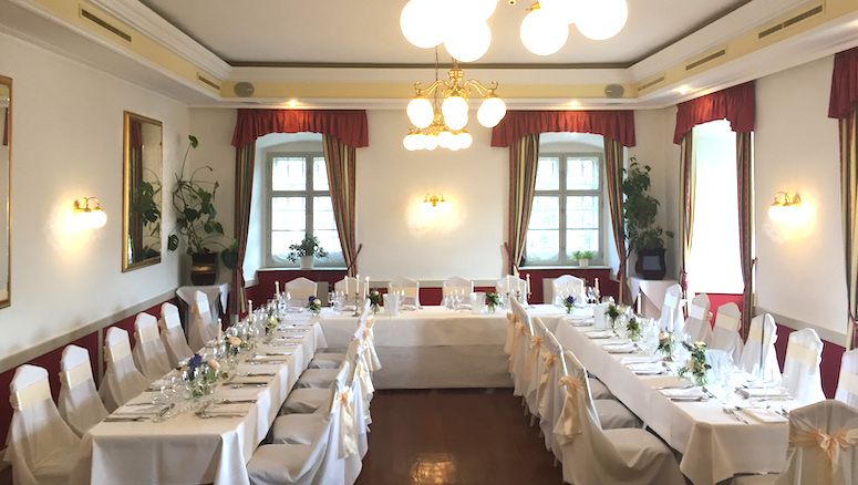 Elegantní sál na zámku Gloggnitz, vyzdobený pro hostinu bílými ubrusy a židlemi.