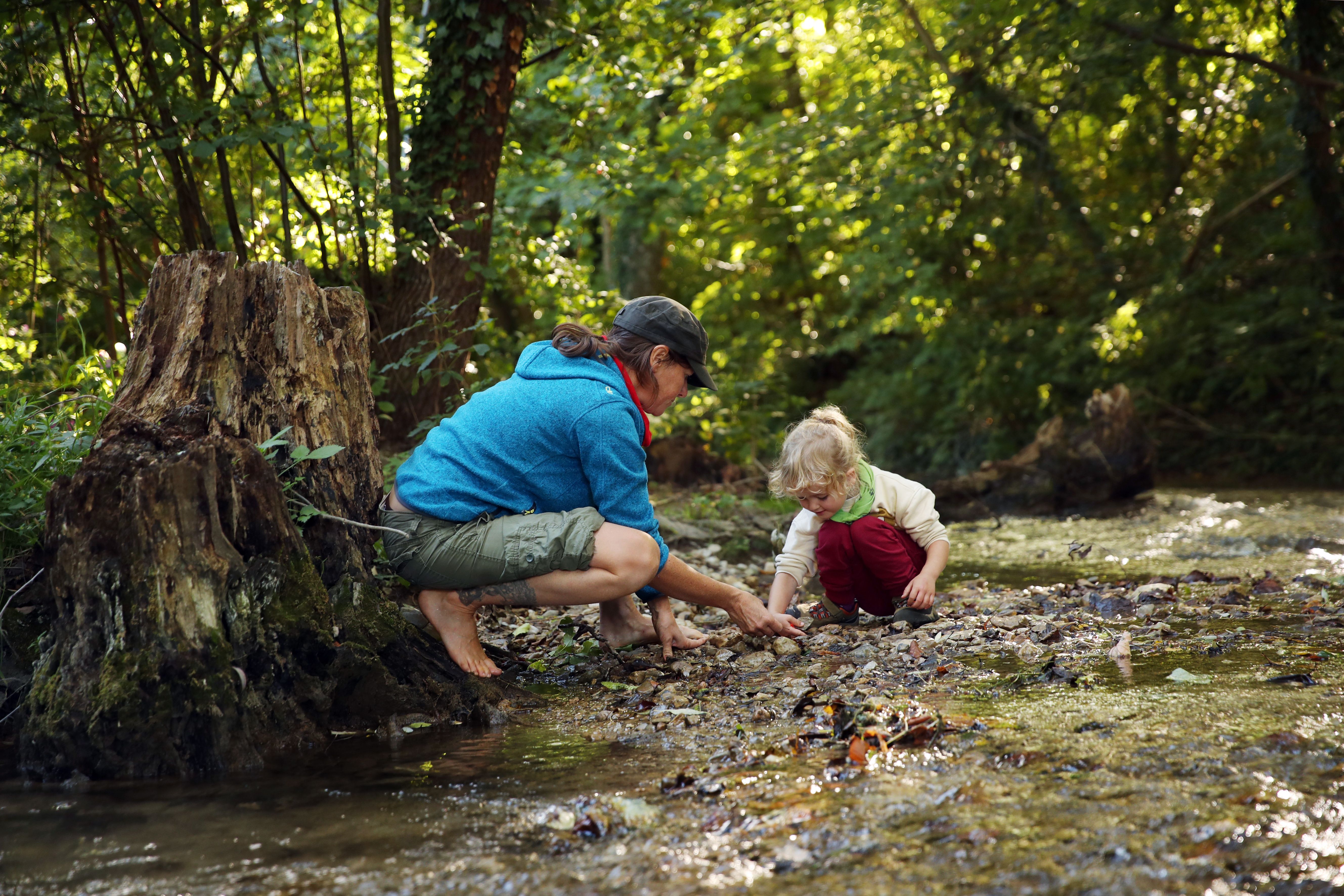 Dospělý a dítě si hrají u potoka v lese.