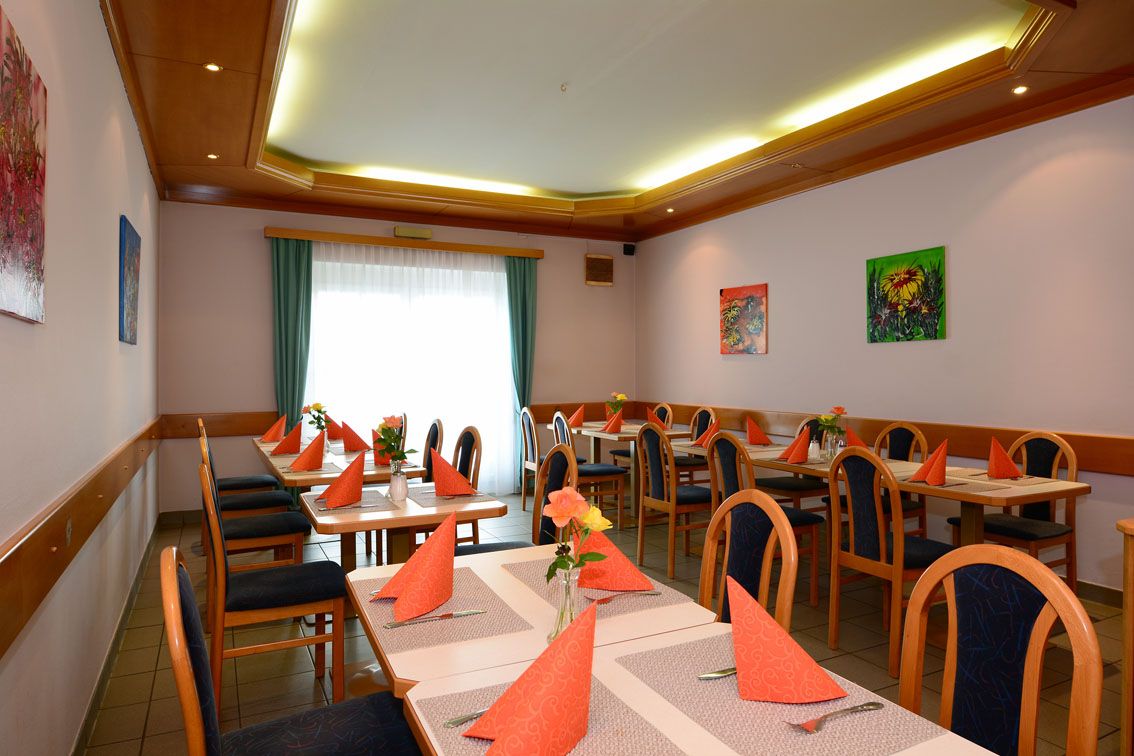 Jídelna s prostřenými stoly, oranžovými ubrousky a vázami s květinami.