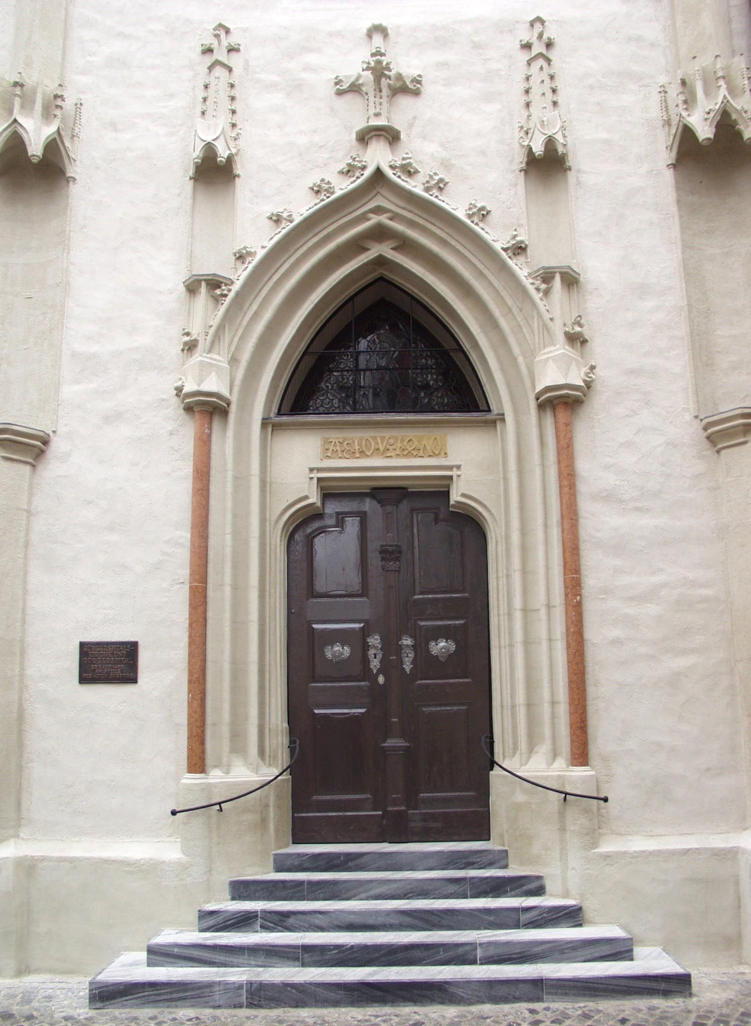 Vchod do kostela Bürgerspitalskirche s gotickým portálem a dřevěnými dveřmi.
