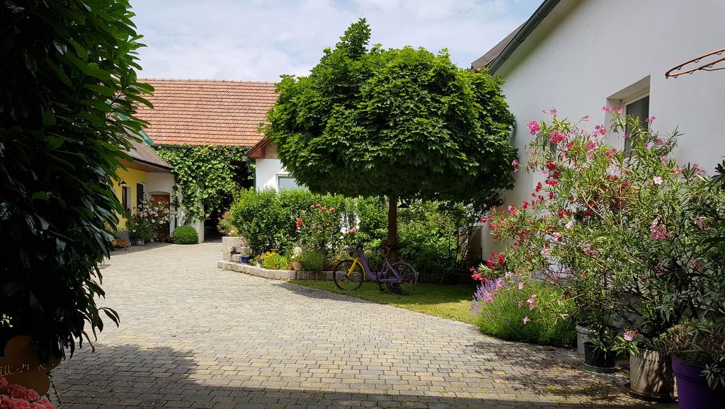 Vnitřní dvůr s dlážděnou cestou, stromy a kvetoucími rostlinami.