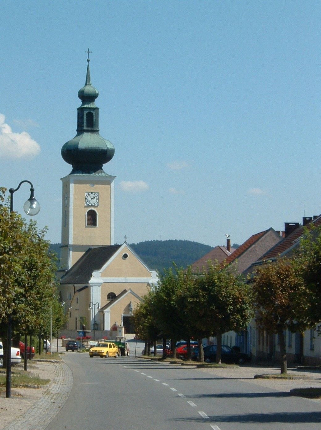 Kostel s cibulovou kopulí v malém městě, obklopený stromy a domy.