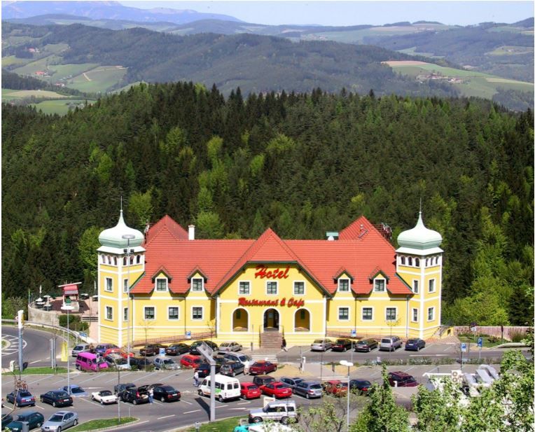 Žlutý hotel s červenými střechami v zelené kopcovité krajině.