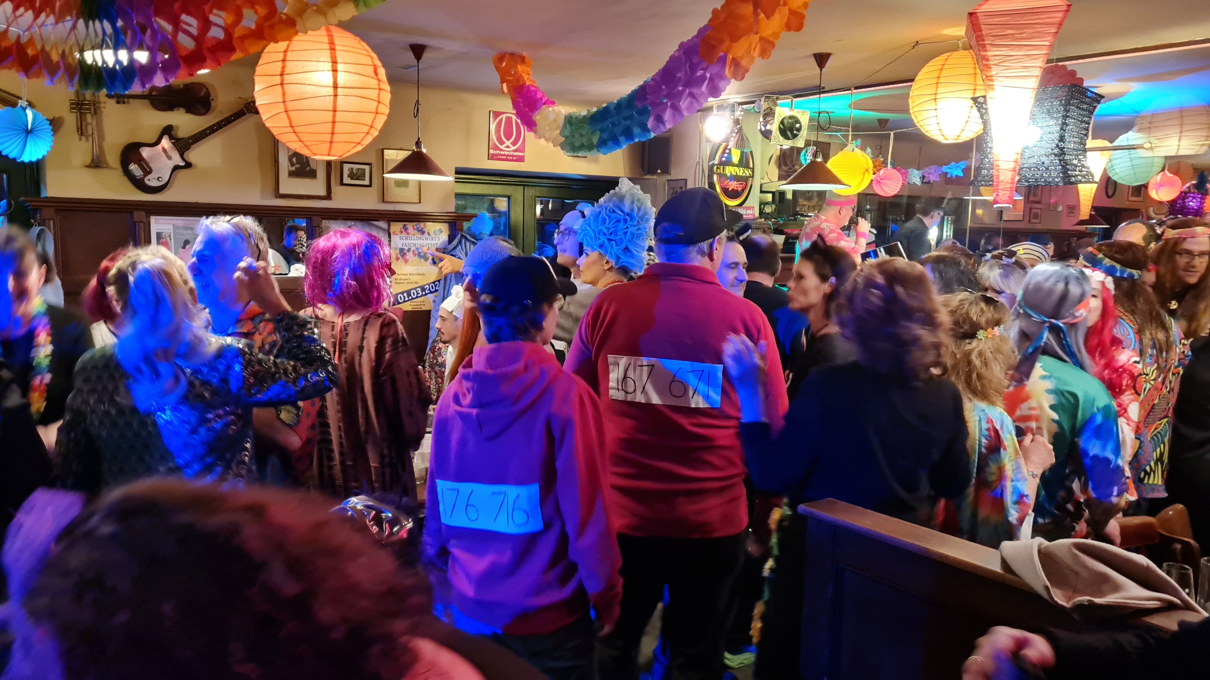 Lidé v pestrých kostýmech slaví karneval ve vyzdobené místnosti.