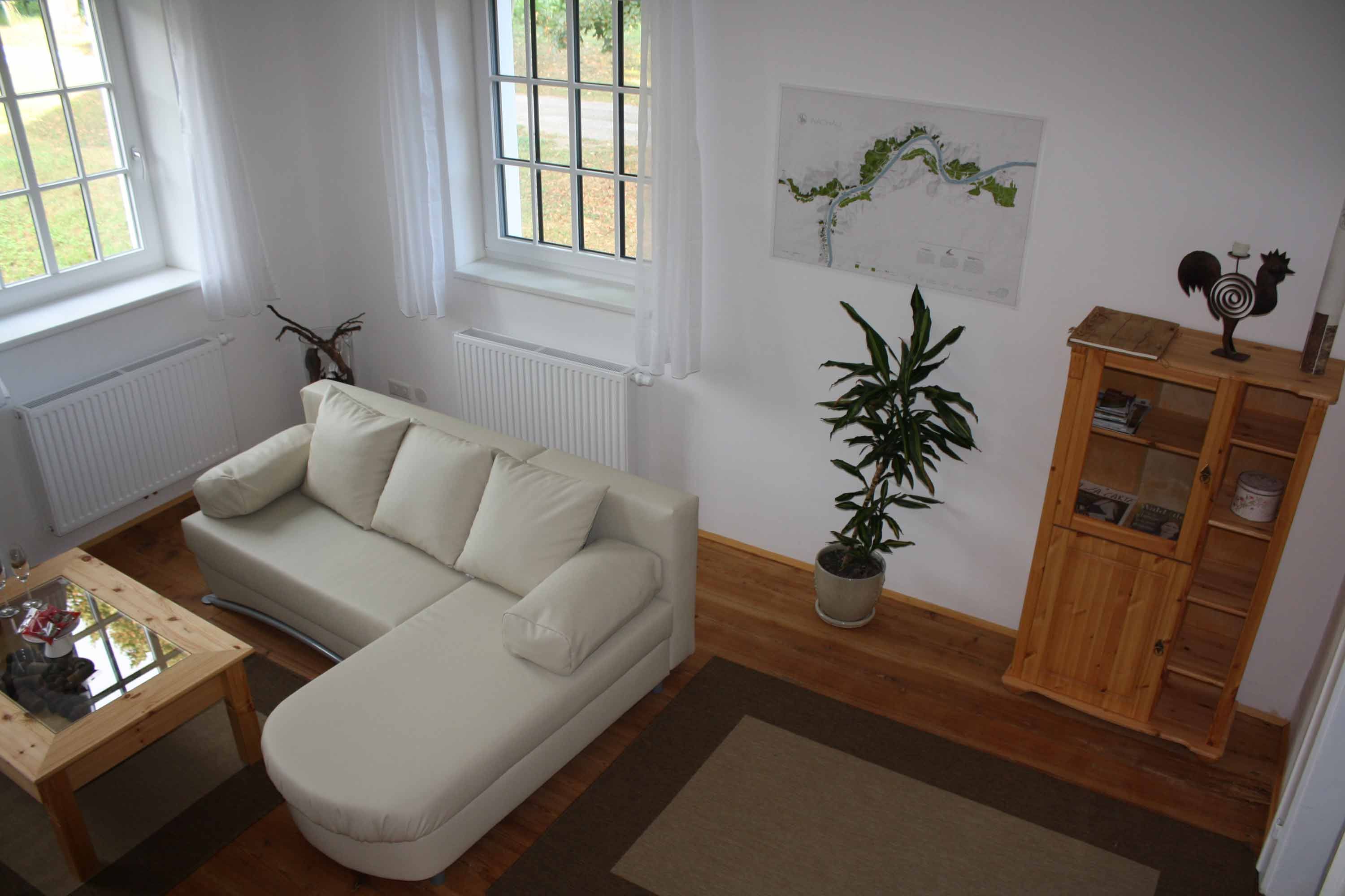 Útulné posezení s béžovou pohovkou, dřevěným stolem, rostlinou a poličkou v rekreačním bytě.