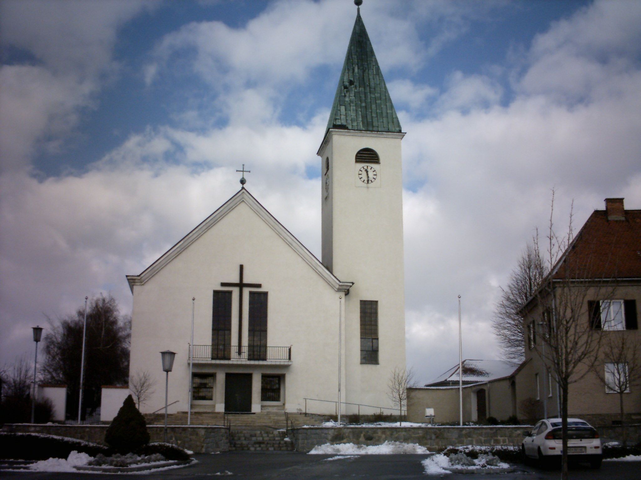 Kostel s věží a hodinami v Sigmundsherbergu, obklopený sněhem a mraky.