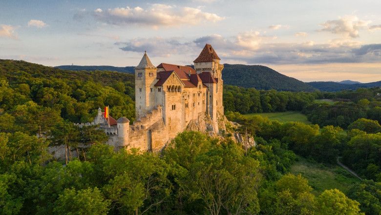 Lichtenštejnský hrad obklopený zelenými lesy při západu slunce.