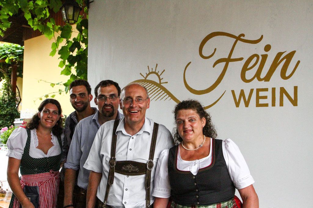 Skupina pěti lidí v tradičním oděvu před nápisem "Fein Wein".