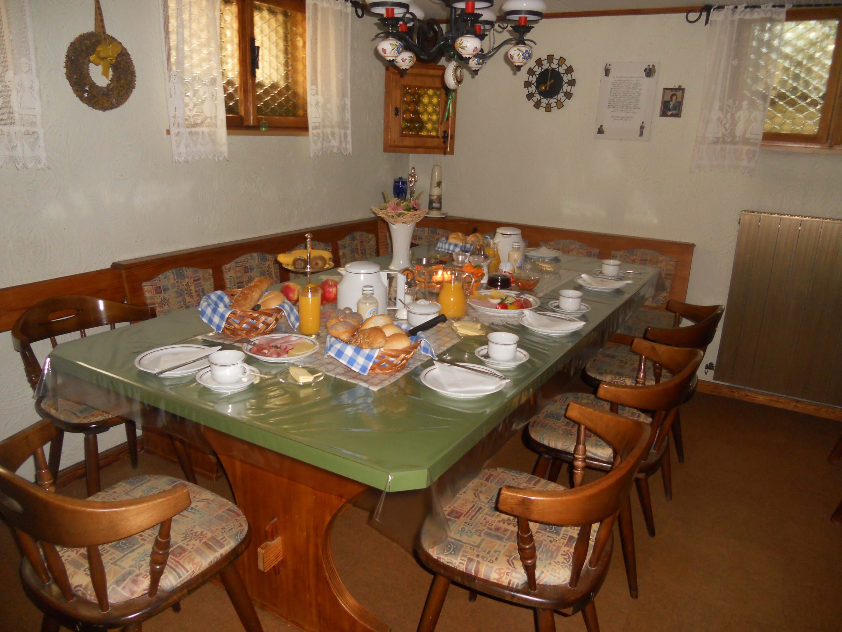 Snídaňová místnost se stolem a židlemi. U stolu se podává bohatá snídaně.