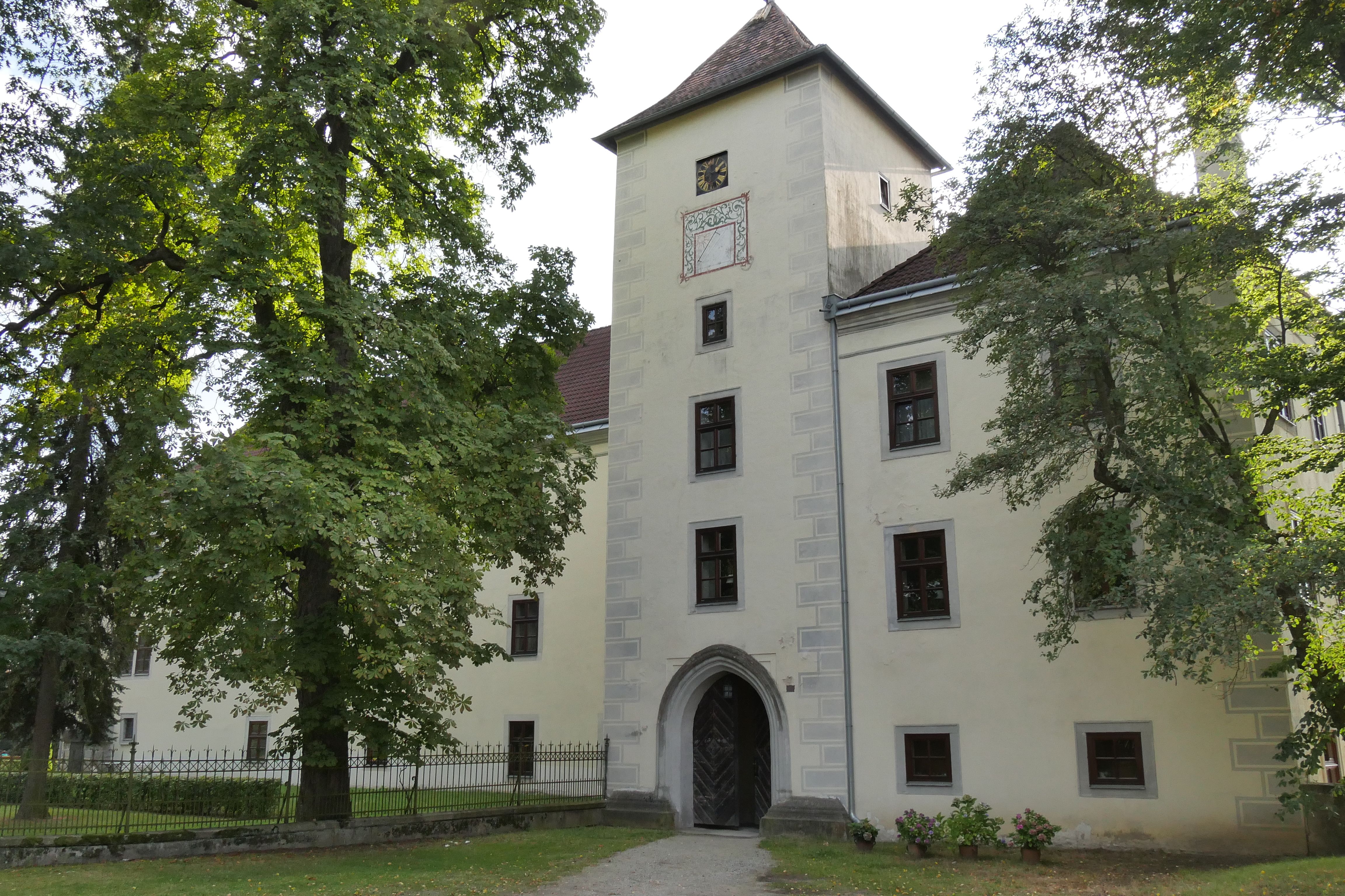 Historická budova s věží a stromy v popředí.