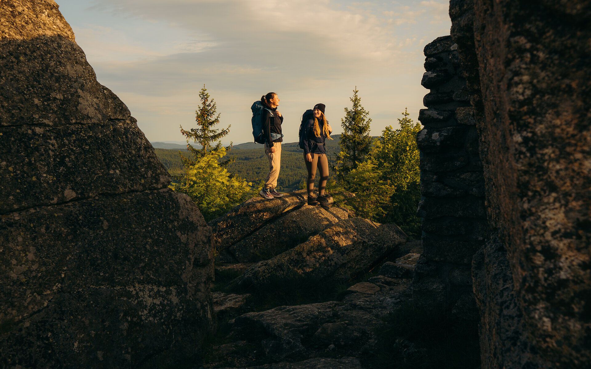 Dva turisté stojí mezi impozantními skalními útvary a ve zlatém ranním světle se kochají výhledem na lesní krajinu ve Waldviertelu.