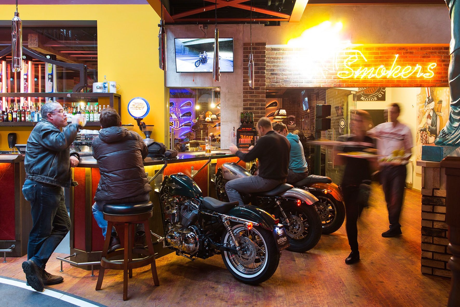 Bar s motocykly jako sedadly, neonovým světlem a hosty.
