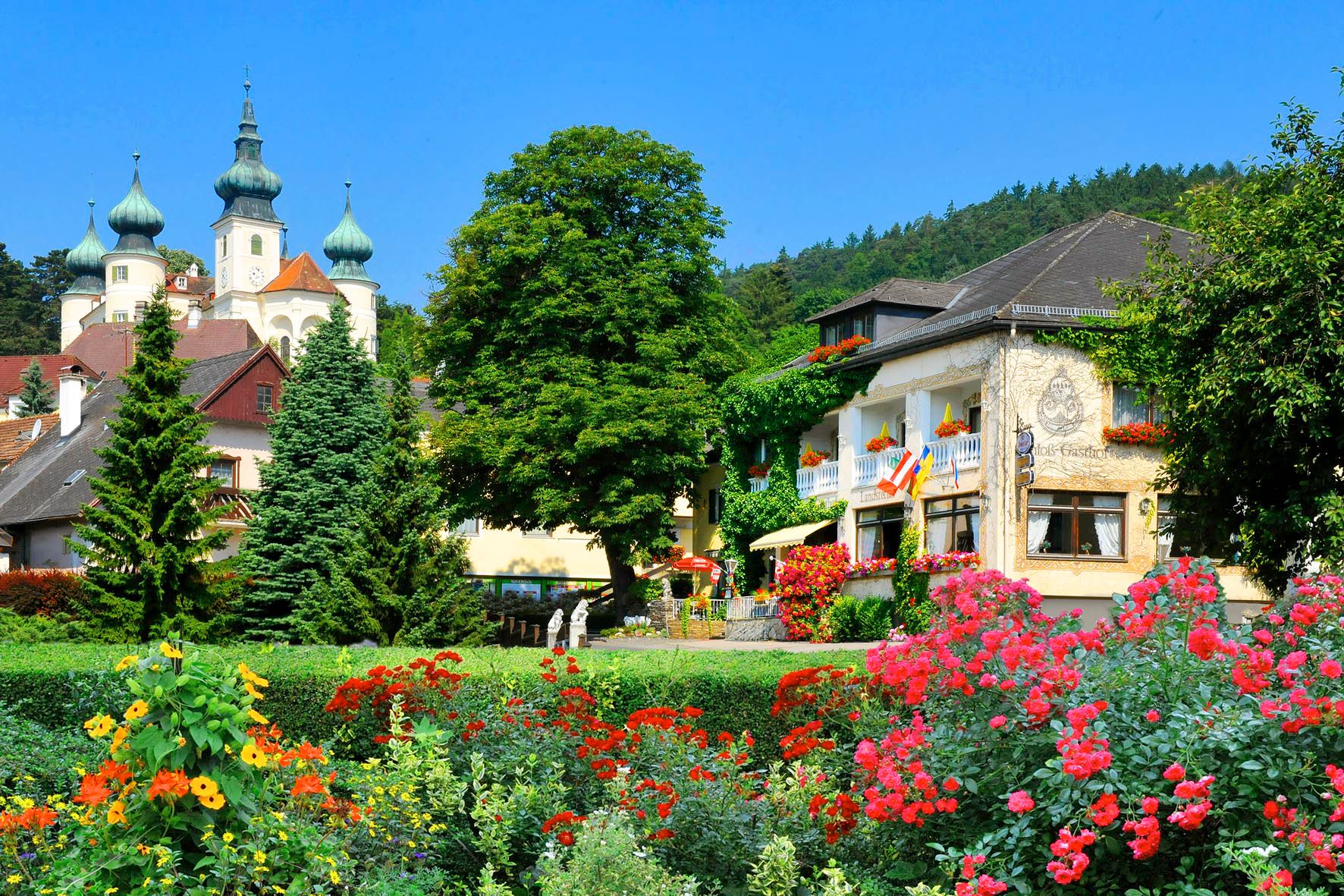 Malebný hotel s barevnými květinami v popředí a hradem v pozadí.
