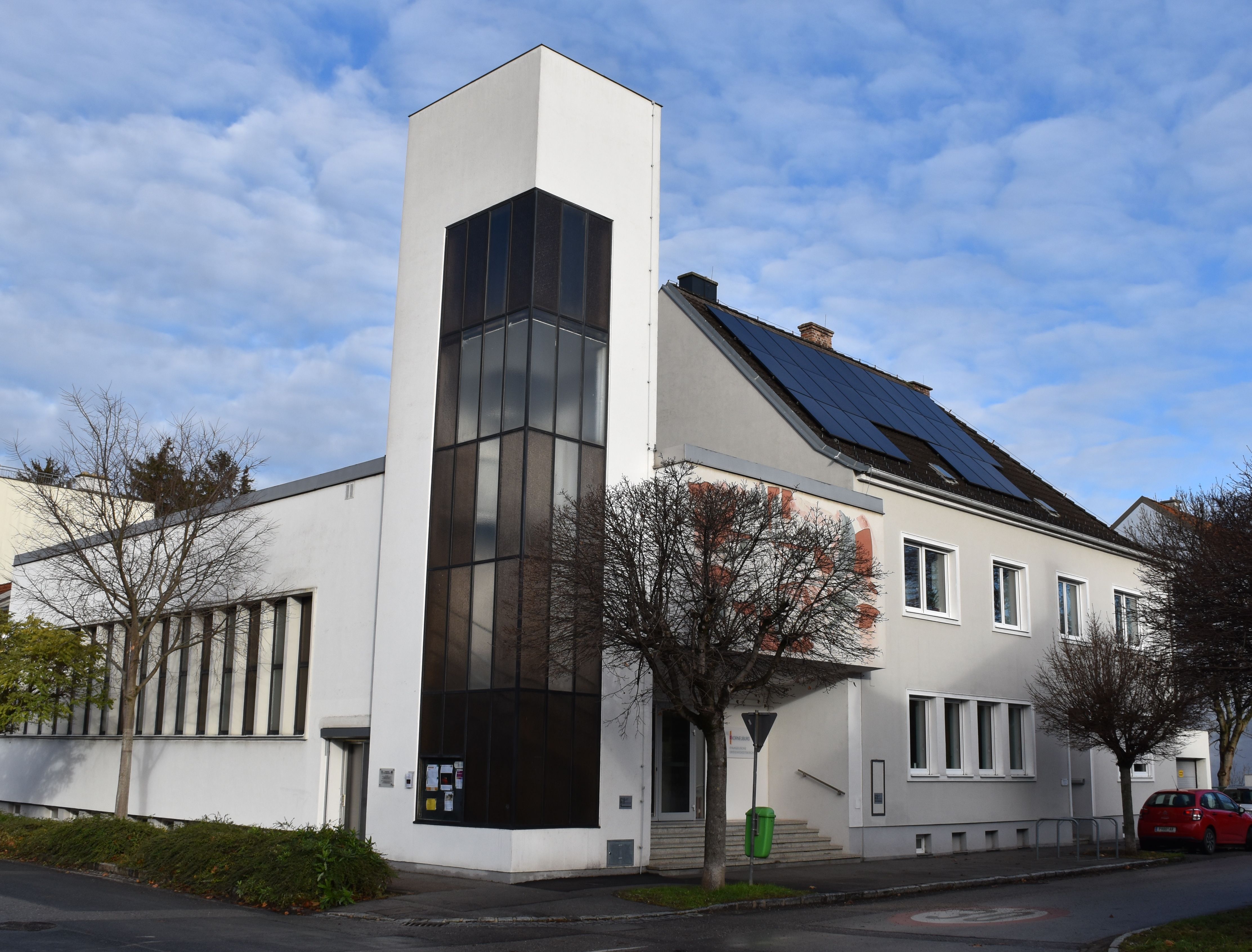 Moderní kostel s bílou fasádou a solárními panely na střeše.