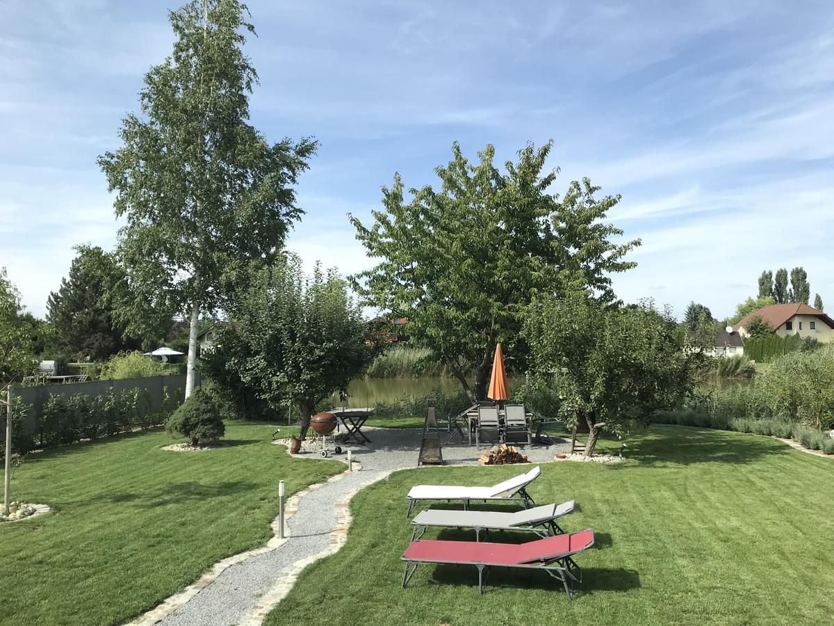 Udržovaná zahrada s trávníkem, stromy, lehátky a stolem se slunečníkem.