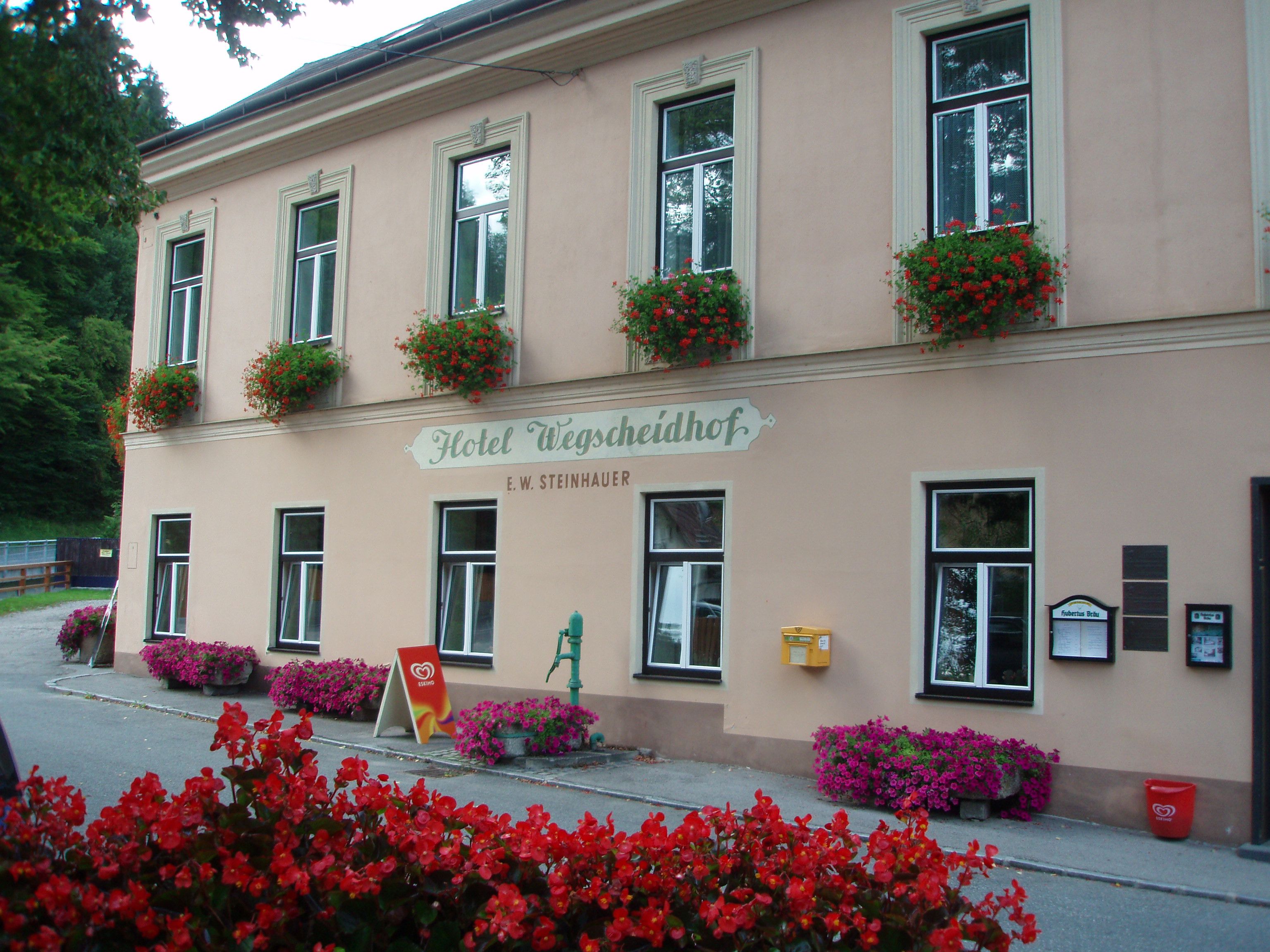 Fasáda hotelu Wegscheidhof s květinovými truhlíky a nápisy.