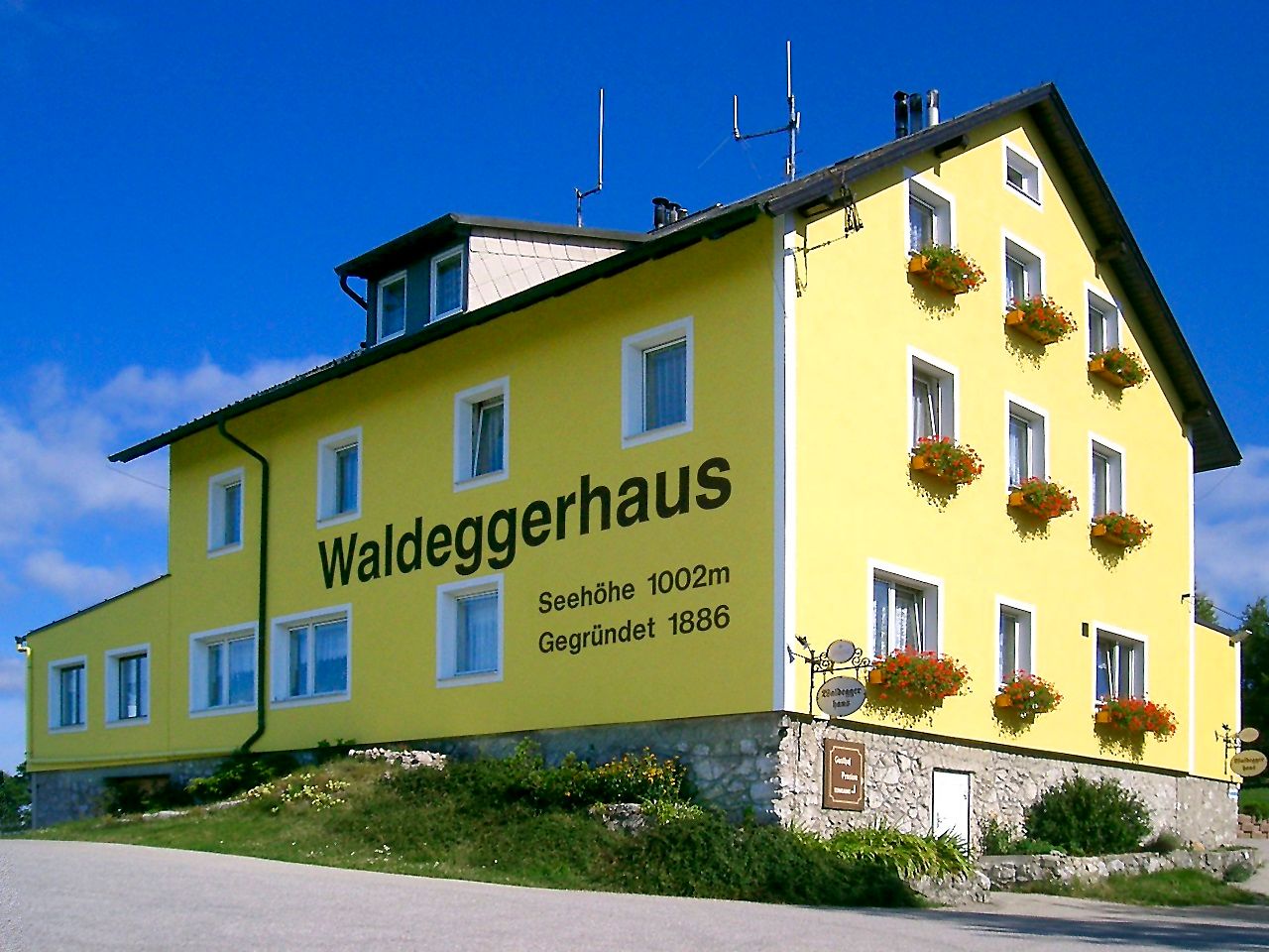 Žlutá budova s nápisem "Waldeggerhaus", obklopená květinami.